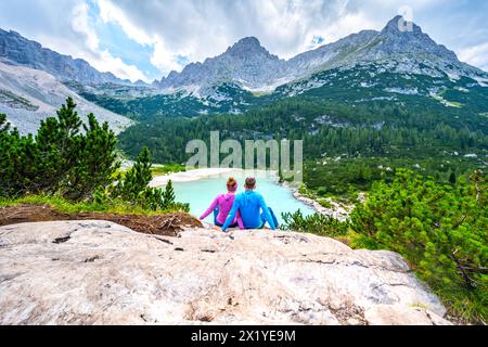 Beschreibung: Junges sportliches Paar genießt am Nachmittag von einem schönen Rastplatz aus den Blick auf den türkisfarbenen Sorapis-See. Sorapissee, Dolomiten, Bel Stockfoto