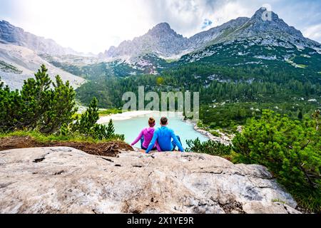 Beschreibung: Junges sportliches Paar genießt am Nachmittag von einem schönen Rastplatz aus den Blick auf den türkisfarbenen Sorapis-See. Sorapissee, Dolomiten, Bel Stockfoto