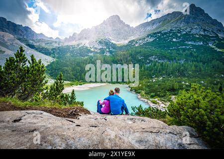 Beschreibung: Junges sportliches Paar genießt am Nachmittag von einem schönen Rastplatz aus den Blick auf den türkisfarbenen Sorapis-See. Sorapissee, Dolomiten, Bel Stockfoto