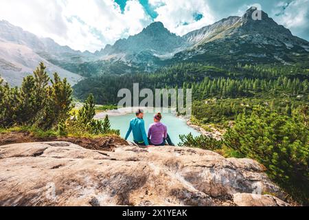 Beschreibung: Junges sportliches Paar genießt am Nachmittag von einem schönen Rastplatz aus den Blick auf den türkisfarbenen Sorapis-See. Sorapissee, Dolomiten, Bel Stockfoto