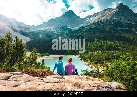 Beschreibung: Junges sportliches Paar genießt am Nachmittag von einem schönen Rastplatz aus den Blick auf den türkisfarbenen Sorapis-See. Sorapissee, Dolomiten, Bel Stockfoto