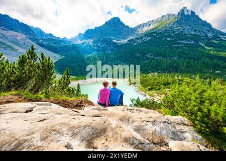 Beschreibung: Junges sportliches Paar genießt am Nachmittag von einem schönen Rastplatz aus den Blick auf den türkisfarbenen Sorapis-See. Sorapissee, Dolomiten, Bel Stockfoto