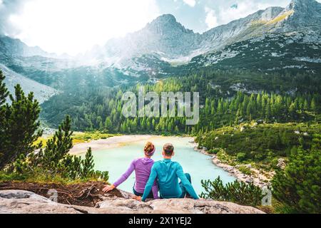 Beschreibung: Junges sportliches Paar genießt am Nachmittag von einem schönen Rastplatz aus den Blick auf den türkisfarbenen Sorapis-See. Sorapissee, Dolomiten, Bel Stockfoto