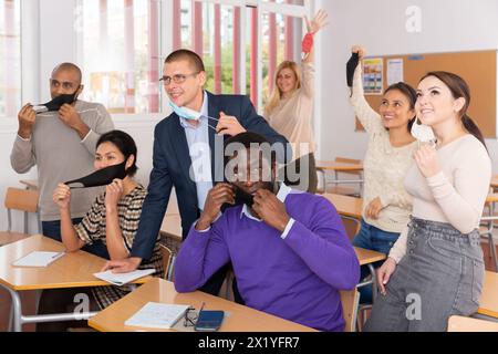 Glückliche Erwachsene Schüler, die Gesichtsschutzmasken im Klassenzimmer abnehmen Stockfoto