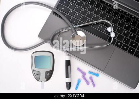 Medizinisches Stethoskop, Diabeteslanzette mit Ersatznadeln, Glucometer, Laptop-Tastatur auf weißem Hintergrund, Ausrüstung für Blutzuckermessung an h Stockfoto