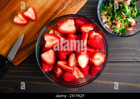 Große Glasschüssel voller gewachsener und halber Erdbeeren: Große Schüssel frischer, reifer Erdbeeren, deren Stiele und Blätter entfernt und in zwei Hälften geschnitten wurden Stockfoto