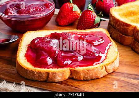 Toastscheibe mit hausgemachten Erdbeerkonserven bedeckt: Geschnittenes und geröstetes Weißbrot und hausgemachte Erdbeerkonserven mit großen Fruchtstücken Stockfoto