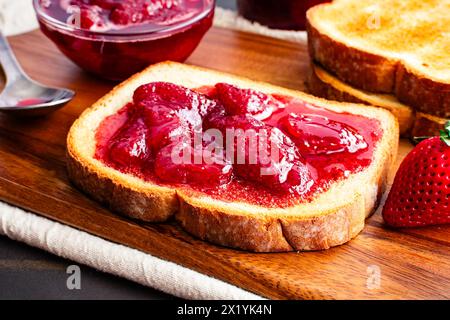 Toastscheibe mit hausgemachten Erdbeerkonserven bedeckt: Geschnittenes und geröstetes Weißbrot und hausgemachte Erdbeerkonserven mit großen Fruchtstücken Stockfoto