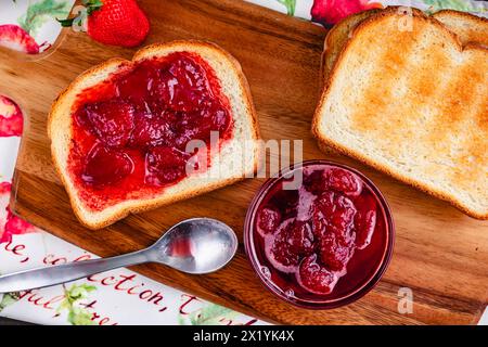 Toastscheibe mit hausgemachten Erdbeerkonserven bedeckt: Geschnittenes und geröstetes Weißbrot und hausgemachte Erdbeerkonserven mit großen Fruchtstücken Stockfoto