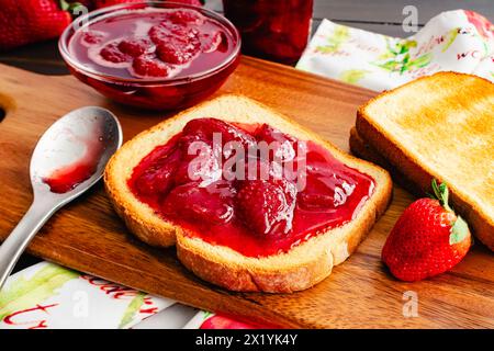 Toastscheibe mit hausgemachten Erdbeerkonserven bedeckt: Geschnittenes und geröstetes Weißbrot und hausgemachte Erdbeerkonserven mit großen Fruchtstücken Stockfoto