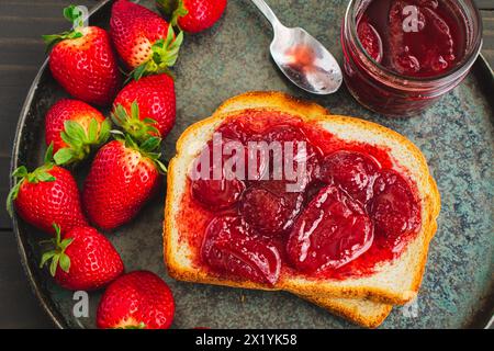 Toastscheibe mit hausgemachten Erdbeerkonserven bedeckt: Geschnittenes und geröstetes Weißbrot und hausgemachte Erdbeerkonserven mit großen Fruchtstücken Stockfoto