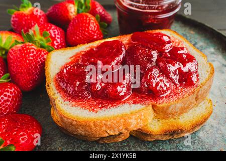 Toastscheibe mit hausgemachten Erdbeerkonserven bedeckt: Geschnittenes und geröstetes Weißbrot und hausgemachte Erdbeerkonserven mit großen Fruchtstücken Stockfoto