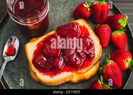 Toastscheibe mit hausgemachten Erdbeerkonserven bedeckt: Geschnittenes und geröstetes Weißbrot und hausgemachte Erdbeerkonserven mit großen Fruchtstücken Stockfoto