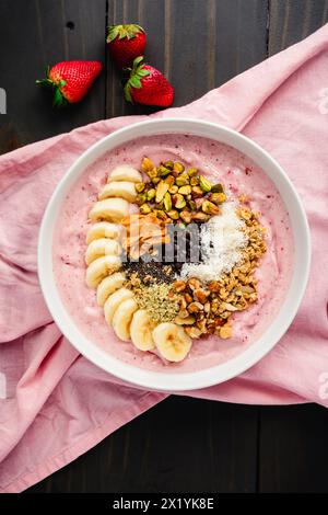Erdbeere Smoothie Bowl voller gesunder Toppings: Fruchtige Schüssel mit Bananenscheiben, Samen, Nüssen, Erdnussbutter und dunklen Schokoladenchips Stockfoto