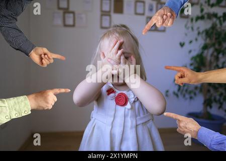 Kleines Kind in einem weißen Kleid, Baby, ein blondes Mädchen steht, bedeckt ihr Gesicht mit ihren Händen vor Groll und Angst, Hände der Familie Anklage, Konzept o Stockfoto