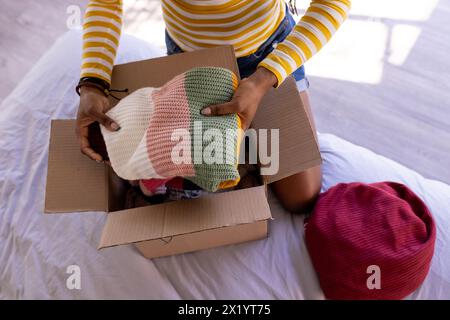 Eine afroamerikanische junge Frau ist zu Hause und packt bunte Strickmützen aus einer Schachtel Stockfoto