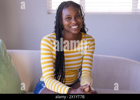 Eine junge afroamerikanische Frau, die zu Hause sitzt und ein gelb gestreiftes Hemd trägt, ist auf einem Videoanruf Stockfoto