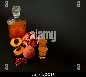 Hausgemachter Obstlikör in einer Glasflasche und zwei Gläsern auf schwarzem Hintergrund, neben reifem Granatapfelstück und gebrochenem Granatapfelfrucht. Oben Stockfoto