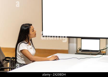 Eine junge Frau steuert eine Präsentation auf dem Bildschirm mit einer Maus mit einem Laptop Stockfoto