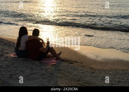 Ein Paar genießt einen Sonnenuntergang bei einem Glas Wein am ruhigen Meer. Stockfoto