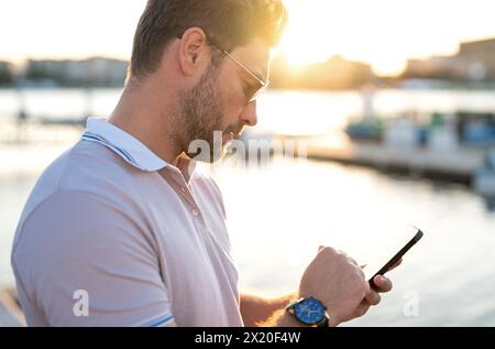 Ein lässiger, gutaussehender Mann, der in der Stadt telefoniert. Gut gekleideter Mann mit modischer Brille und Polo, der draußen telefoniert. Geschäftsmann Stockfoto