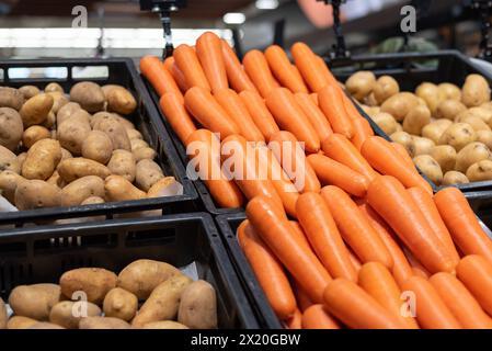 Ein Berg von Karotten neben Kartoffeln im Gemüsebereich eines Lebensmittelgeschäfts. Stockfoto