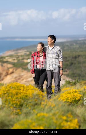 Ein Paar, das auf einem Hügel stand und einen wunderschönen Blick auf das Meer hatte. Der Mann trägt ein kariertes Hemd und die Frau ein rotes kariertes Hemd Stockfoto