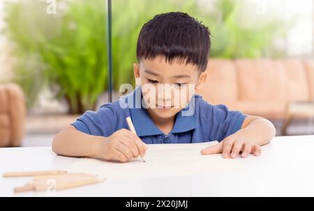 Lächelnder asiatischer Schuljunge, der zu Hause studiert und schreibt Stockfoto