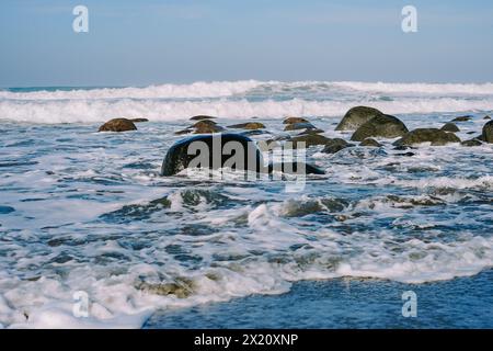 Die Ruhe am Morgen wird in einem ruhigen Küstenbild mit kleinen Wellen, felsigem Strand und der beruhigenden Aura des Sonnenaufgangs aufgenommen Stockfoto
