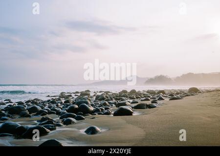 Die Ruhe am Morgen wird in einem ruhigen Küstenbild mit kleinen Wellen, felsigem Strand und der beruhigenden Aura des Sonnenaufgangs aufgenommen Stockfoto