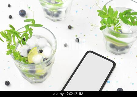 Sommergetränke und Telefon mit leerem Platz zum Füllen von Inhalten. Grüne und dunkelblaue Dekorationen, Draufsicht. Stockfoto