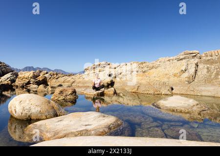 Birassische Wanderer sitzt auf Felsen, reflektiert im Wasser, Kopierraum Stockfoto