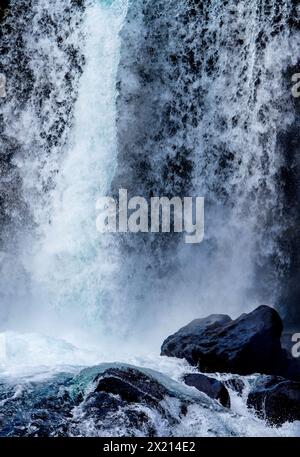 Ein Wasserfall mit einem Felsen davor. Das Wasser ist weiß und der Felsen schwarz Stockfoto