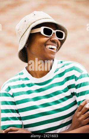 Draußen Porträt einer jungen, fröhlichen Frau mit Sonnenbrille und Hut. Eine junge Frau lächelt fröhlich im Freien. Stockfoto