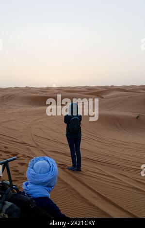 Weibliche Touristen bewundern den Sonnenaufgang in der Wüste Merzouga mit einem trüben Himmel über dem weiten Sand. Stockfoto