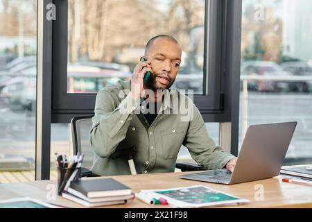 Schwarzer Mann sitzt an einem Schreibtisch, voll verwickelt in einen Anruf mit dem Handy, tief im Gespräch. Stockfoto