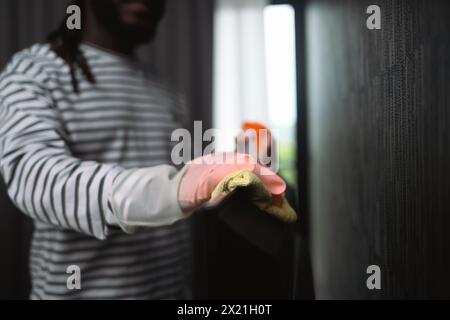 Abgeschnittene Aufnahme eines jungen Afrikaners, der mit Mikrofasertuch den Staub vom Fernseher abwischt Stockfoto