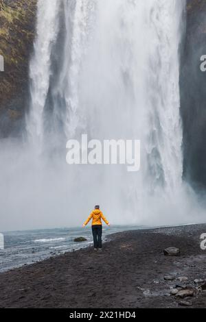 Ein einsamer Abenteurer in Gelb steht der rohen Kraft des Skogafoss Tow gegenüber Stockfoto