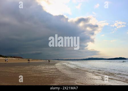 Am späten Nachmittag taucht die September-Sonne durch die schwere dunkle Wolke auf, mit Spaziergängern in der seichten Brandung am Somo Beach Ribamontán al Mar Cantabria Spanien Stockfoto