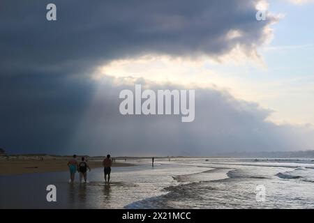 Am späten Nachmittag taucht die September-Sonne durch die schwere dunkle Wolke auf, mit Spaziergängern in der seichten Brandung am Somo Beach Ribamontán al Mar Cantabria Spanien Stockfoto