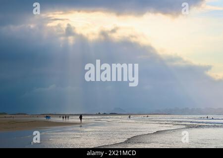 Am späten Nachmittag taucht die September-Sonne durch die schwere dunkle Wolke auf, mit Spaziergängern in der seichten Brandung am Somo Beach Ribamontán al Mar Cantabria Spanien Stockfoto