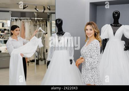 Junge Frau, die im Salon ein Hochzeitskleid aussucht. Die zukünftige Braut kam in einen Brautkleidersalon, um ein Kleid zu kaufen. Stockfoto