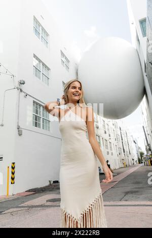 Eine junge blonde Frau in einem fließenden weißen Kleid in der Nähe eines großen weißen Balls, die Schönheit und Anmut ausstrahlt. Stockfoto