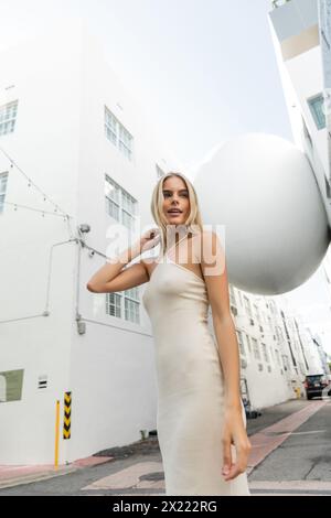 Eine atemberaubende blonde Frau in einem fließenden weißen Kleid posiert für ein Bild in einer lebhaften Miami-Umgebung. Stockfoto