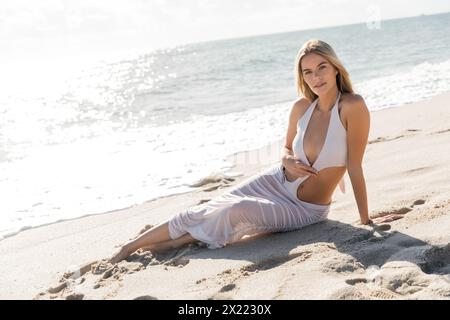 Eine atemberaubende blonde Frau liegt friedlich auf einem Sandstrand in Miami und verkörpert Ruhe und Entspannung. Stockfoto