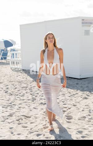 Eine junge blonde Frau steht anmutig an einem Sandstrand, umgeben von der beruhigenden Weite der Küste von Miami. Stockfoto