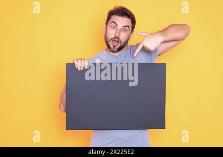 Ein Mann, der Werbung zeigt und mit dem Finger auf eine leere Tafel zeigt, im Studiohintergrund. Leeres Schild mit Textbereich. Werbekonzept. Anzeigetafel mit Stockfoto