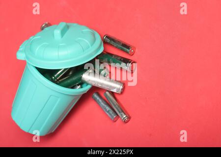 Gebrauchte Fingerbatterien in einem Miniatur-Mülleimer. Rosafarbener Hintergrund. Feld für Text. Stockfoto