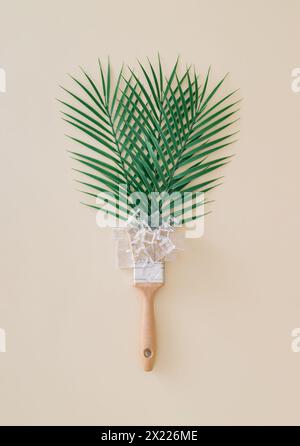 Kreatives Sommerlayout mit grünen Palmenblättern, Eiswürfeln und Pinsel auf sandfarbenem Hintergrund. Minimales tropisches Sommerkonzept. Stockfoto