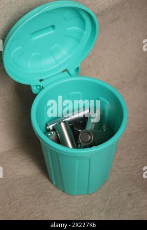 Gebrauchte Fingerbatterien in einem Miniatur-Mülleimer. Auf einem beigefarbenen schmutzigen Hintergrund. Stockfoto